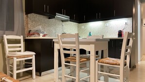 A modern kitchen with white chairs, a black countertop, and a tiled backsplash. - Milo by the sea (Analipsi)