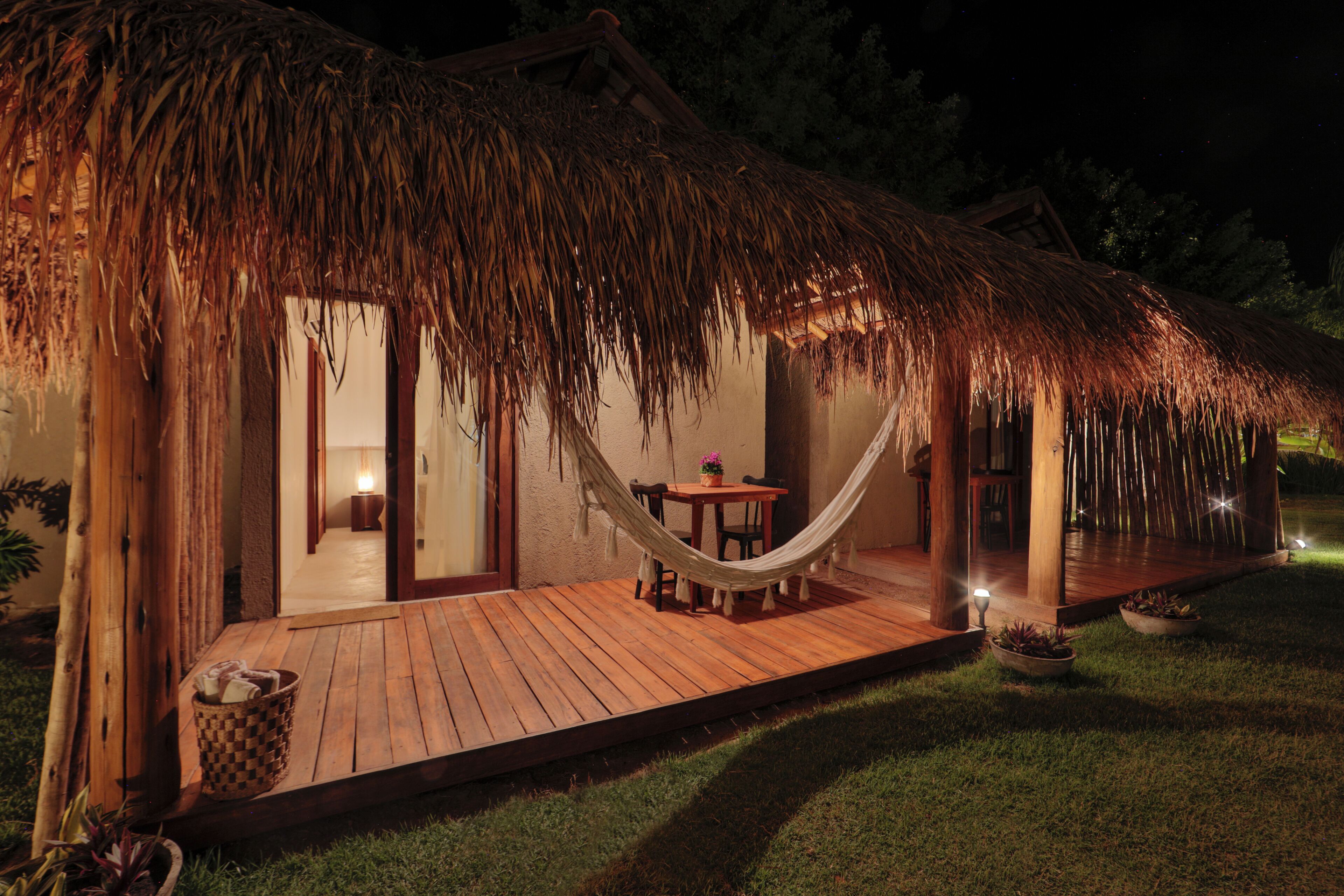 A thatched-roof structure with a wooden deck, a hammock, and a small table with chairs.