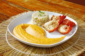 Savor a delicious meal on a woven mat, featuring a generous serving of rice, grilled lobster, and fresh mango.