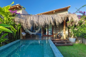 Relax by the tranquil pool surrounded by lush greenery and a thatched roof structure.