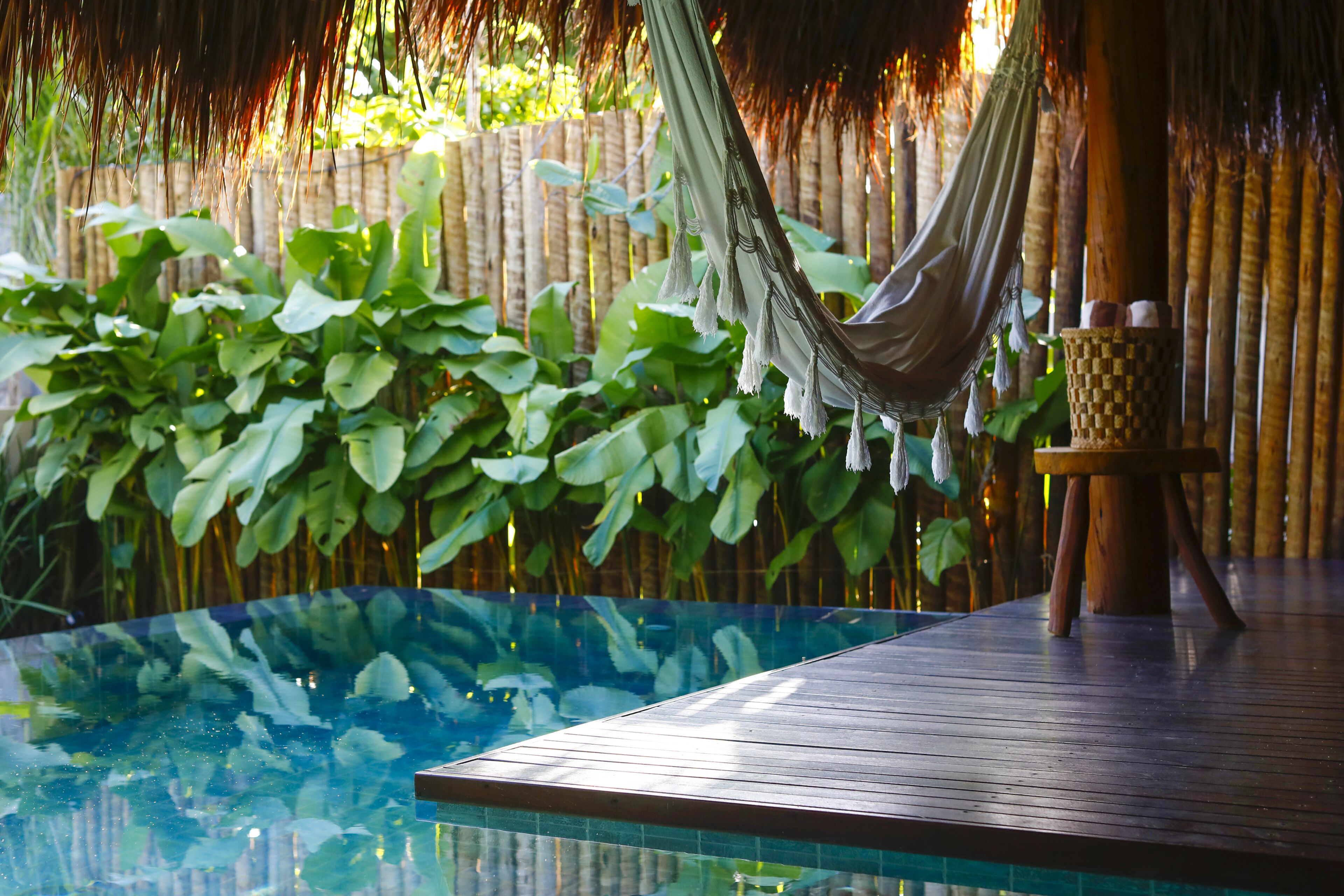 A wooden deck with a glass-bottomed pool, a hammock, and lush green foliage in the background.