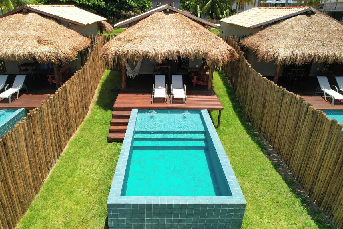 A pool area with a wooden deck, lounge chairs, and thatched-roof structures.