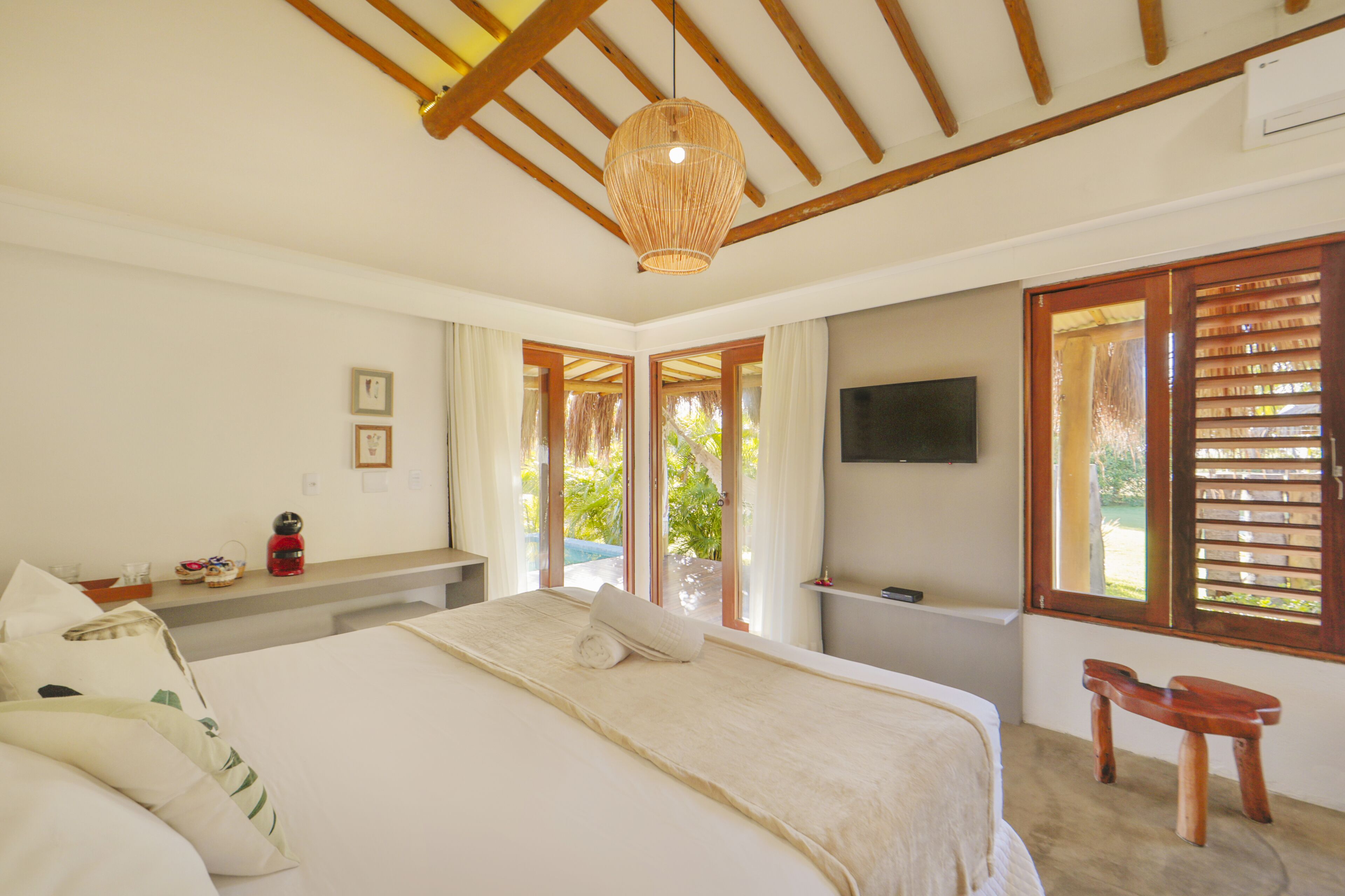 A bedroom with a large bed, a wooden ceiling, a television, and a window with shutters.