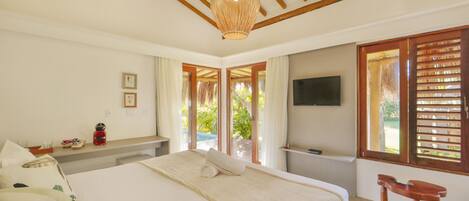 A bedroom with a large bed, a wooden ceiling, a television, and a window with shutters.