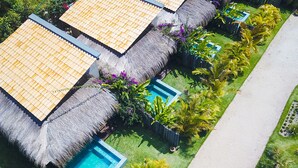 Um resort com construções de telhado de palha, piscina e vegetação exuberante.