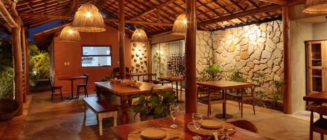 A restaurant with wooden tables and chairs, hanging lamps, and a stone wall.
