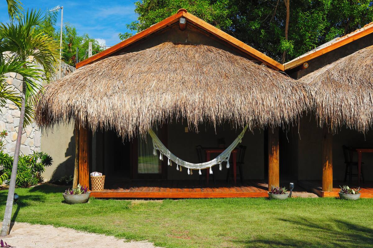 A thatched-roof building with a hammock, potted plants, and a stone wall.