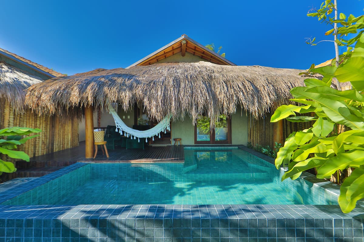 A pool area with a thatched roof structure, a hammock, and a tiled pool.