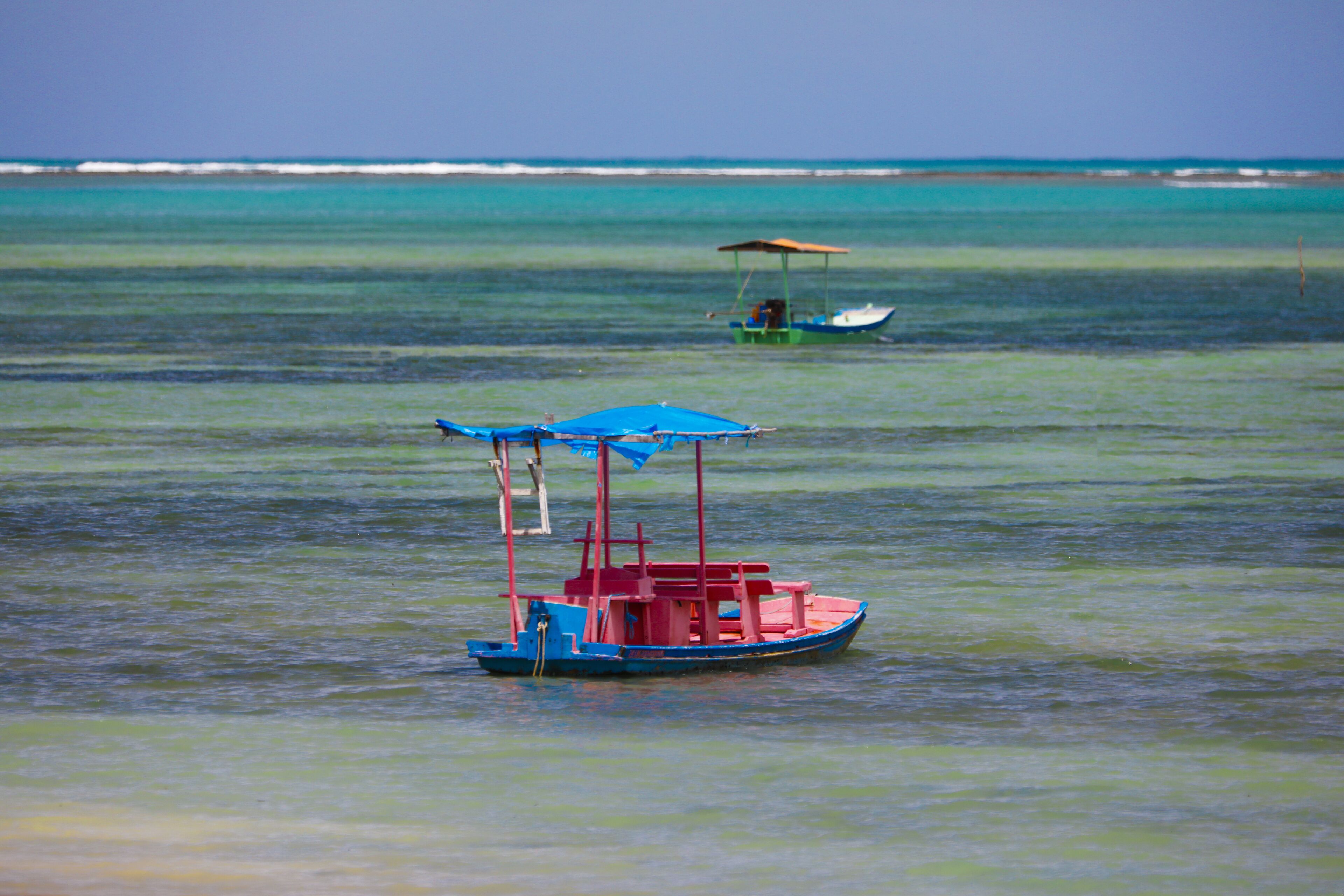 A small boat with a blue canopy and a red structure floating on calm water.