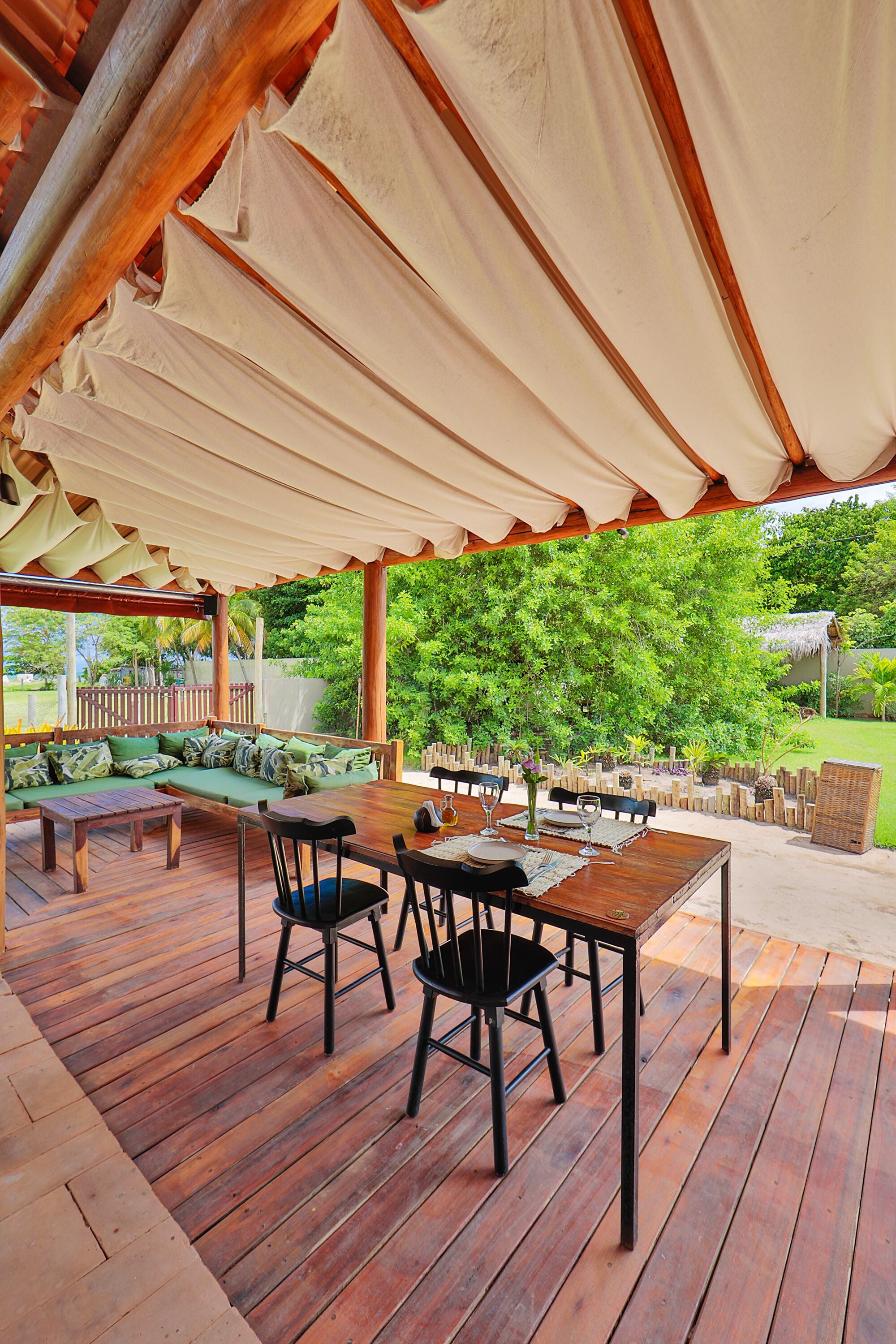 Eine Außenpatio mit Holzmöbeln, einem überdachten Sitzbereich und Blick auf einen üppigen Garten.