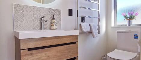 A modern bathroom with a wooden vanity, a round mirror, a towel rack, and a toilet.