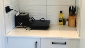 Una cocina compacta con un armario blanco, un tostador negro, una botella de aceite de cocina y un bloque de cuchillos.