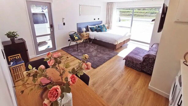 Una habitación de hotel moderna con una cama, un escritorio, una silla y un ventanal grande.