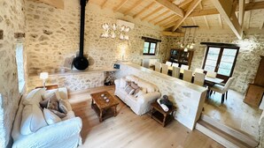 A rustic stone-walled room with a fireplace, wooden ceiling beams, a sofa, a coffee table, and a dining area with chairs and a table. - 7 bed house in idyllic location with heated pool, hot tub, gym, games room & A/C (Massoulès)