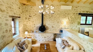 A rustic interior with stone walls, wooden beams, a central fireplace, two sofas, a coffee table, and a hanging light fixture. - 7 bed house in idyllic location with heated pool, hot tub, gym, games room & A/C (Massoulès)