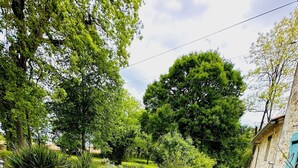 A patio area with wicker furniture, a stone wall, and a view of a lush garden. - 7 bed house in idyllic location with heated pool, hot tub, gym, games room & A/C (Massoulès)