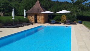 A rectangular swimming pool with a stone border, surrounded by lounge chairs and umbrellas, with a stone building in the background.
