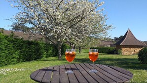 A wooden table with two glasses of red wine in a garden with a stone building in the background.
