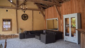 A rustic interior with a wooden ceiling, a large mirror, a dark sofa set, and a cabinet with glass doors.
