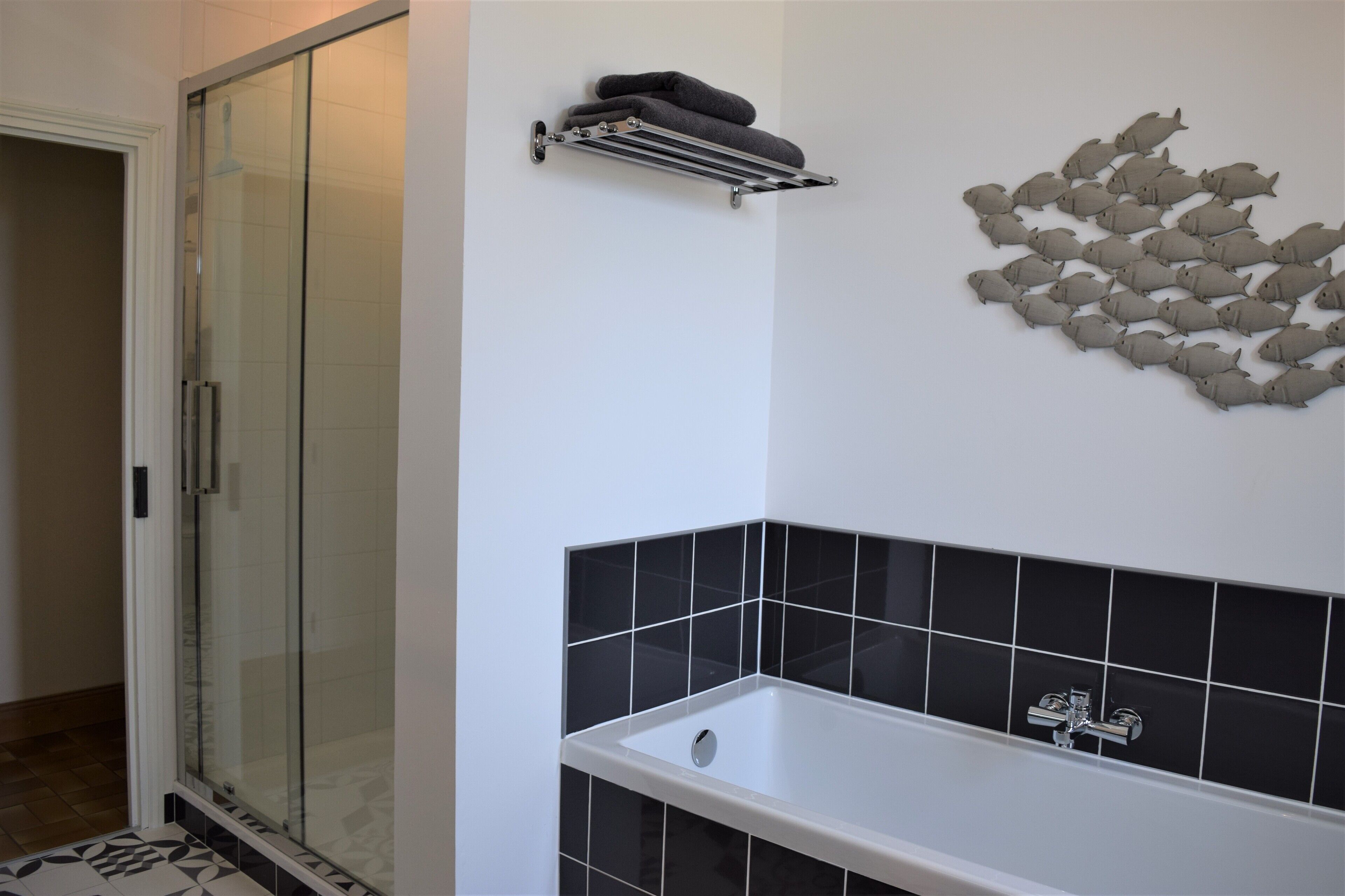 Casa de banho com cabine de duche em vidro, banheira com azulejos pretos e um porta-toalhas com toalhas.