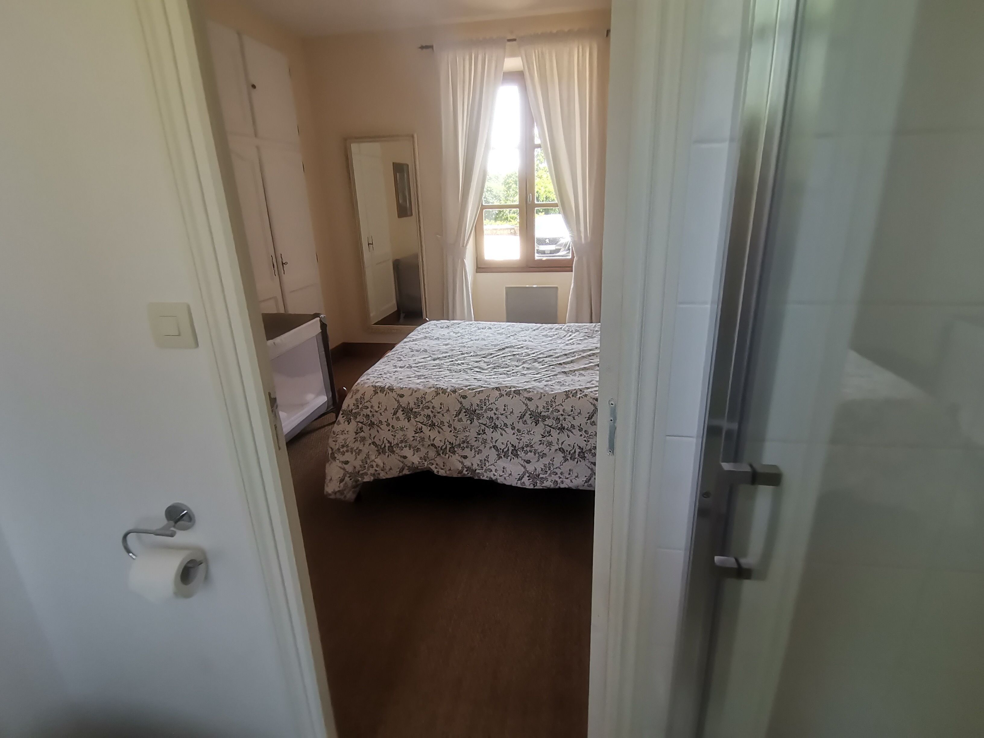 A bedroom with a bed, a wardrobe, a mirror, and a window with curtains.