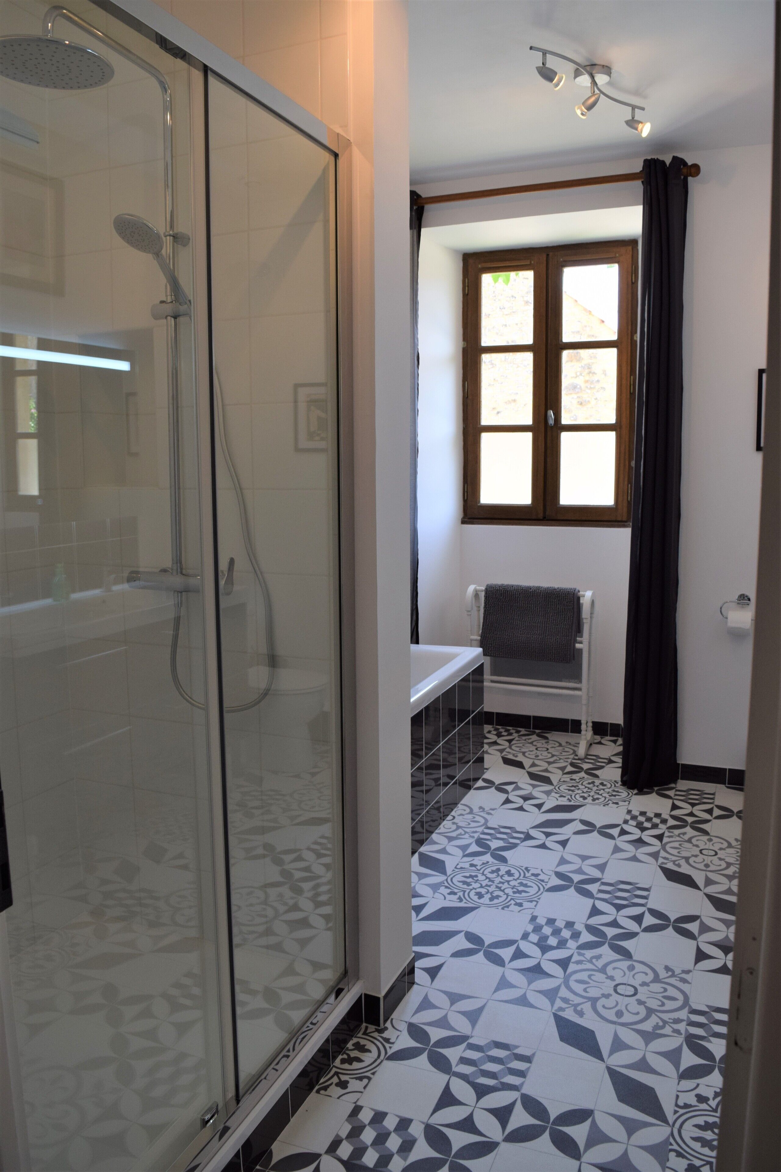 Une salle de bain avec une douche à parois de verre, une fenêtre avec des rideaux et des carreaux de sol à motifs.