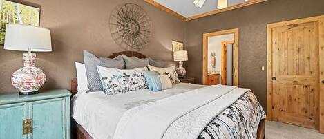 Une chambre à coucher comprenant un lit, des tables de chevet, une commode, un élément décoratif mural et une porte en bois.