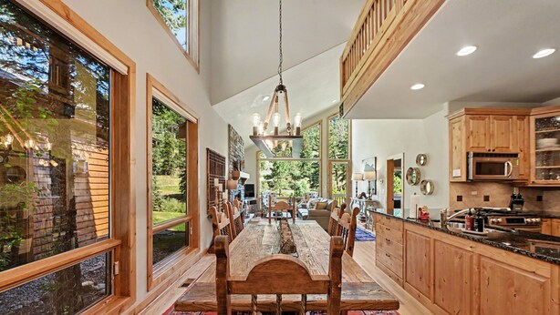 A spacious kitchen with wooden cabinets, a dining area with a large table, and large windows offering views of the outdoors.