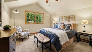 A bedroom with a bed, a chair, a desk, a window, and a ceiling fan.