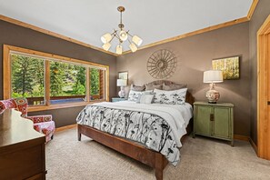 A bedroom with a large bed, a window with a view of greenery, a chandelier, and a green nightstand.