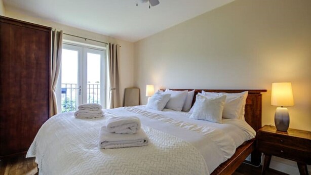 Una habitación de hotel con una cama grande, dos lámparas de noche, un ventilador de techo y vistas al exterior a través de una ventana.