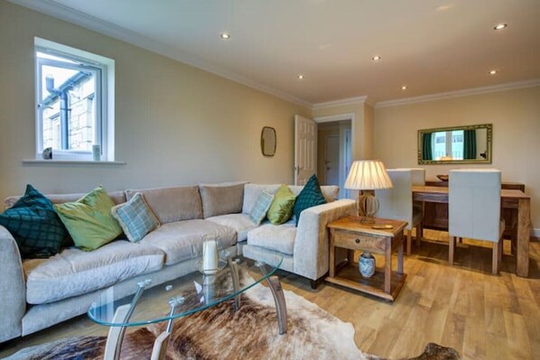 A living room with a sofa, glass coffee table, and a rug. There is a dining area with a table and chairs. - Inglewood Apartment Yorkshire Dales National Park 3 Peaks & Lake District (Ingleton)