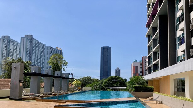 A rooftop pool area with lounge chairs and a table, surrounded by high-rise buildings. - La Santir by PSR (Pattaya)