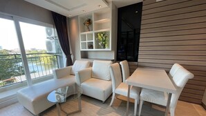 A modern living room with a sofa set, a glass coffee table, and a dining table. There is a large window with a view of a balcony and a cityscape. - La Santir by PSR (Pattaya)
