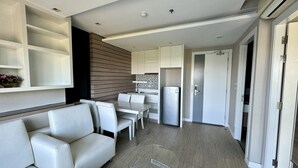 A modern living room with a sofa, a glass coffee table, and a kitchen area with cabinets and a refrigerator. - La Santir by PSR (Pattaya)