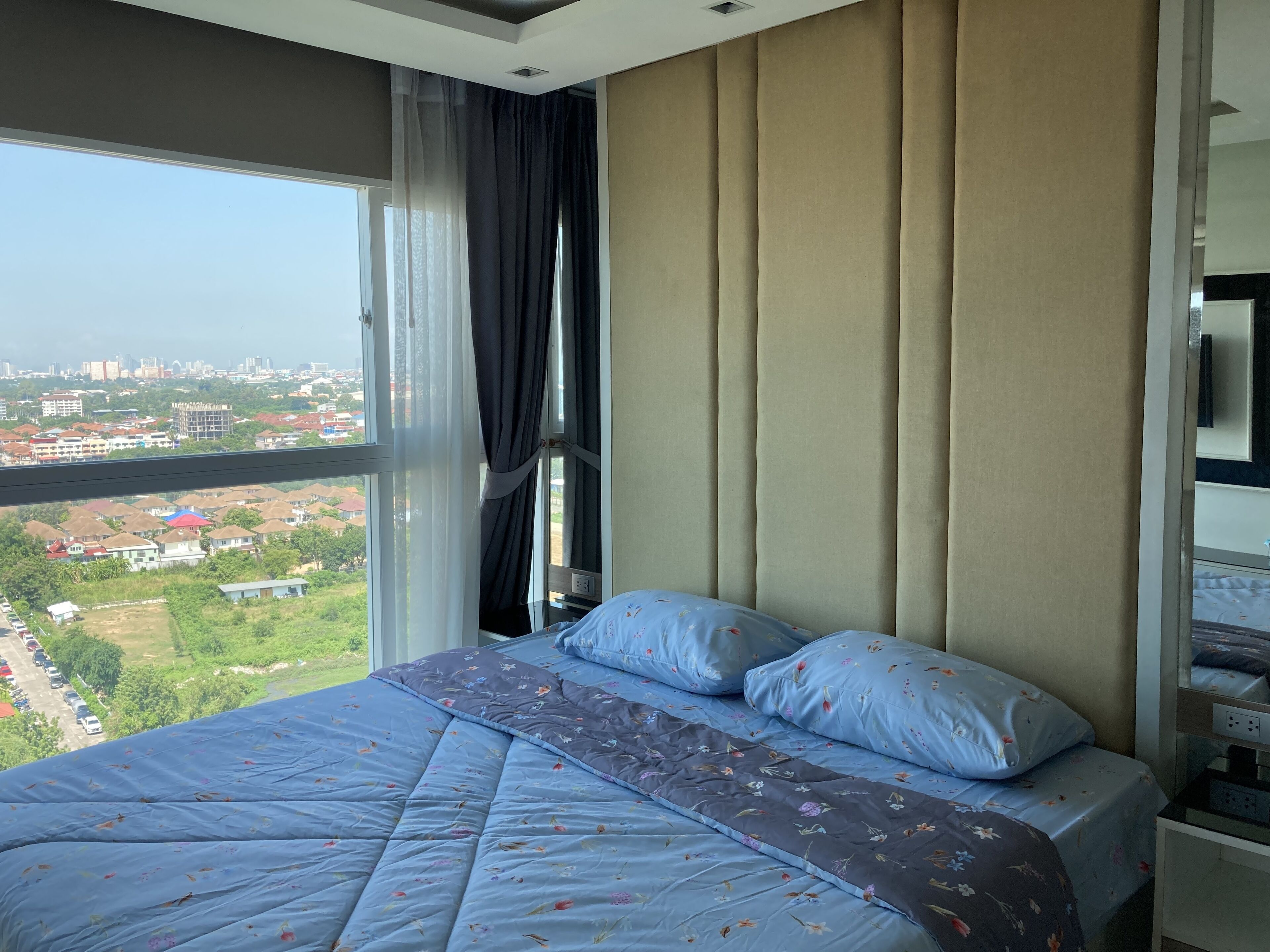 A bedroom with a large bed, a window with curtains, and a city view.