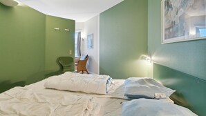 Habitació d'hotel amb un llit, una cadira, un quadre i una finestra.