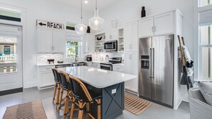 A modern kitchen with white cabinetry, stainless steel appliances, and a central island with bar stools. - BVR 61 - The Good Life by Liquid Life (Orange Beach)