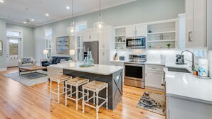 Cocina moderna con armarios blancos, electrodomésticos de acero inoxidable y una isla central con taburetes.