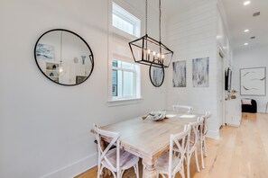 A modern dining area with a wooden table and white chairs, a round mirror, and abstract wall art.
