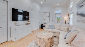 A spacious living room with a large flat-screen TV, a round coffee table, and a beige sofa.