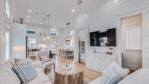 A spacious living room with a large TV, a wooden coffee table, and a dining area with a kitchen in the background.