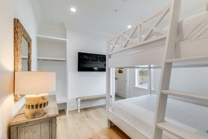 A bedroom with a bunk bed, a bedside table with a lamp, a wall-mounted mirror, and a framed picture.