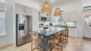 A modern kitchen with white cabinetry, stainless steel appliances, a central island with bar stools, and pendant lighting.