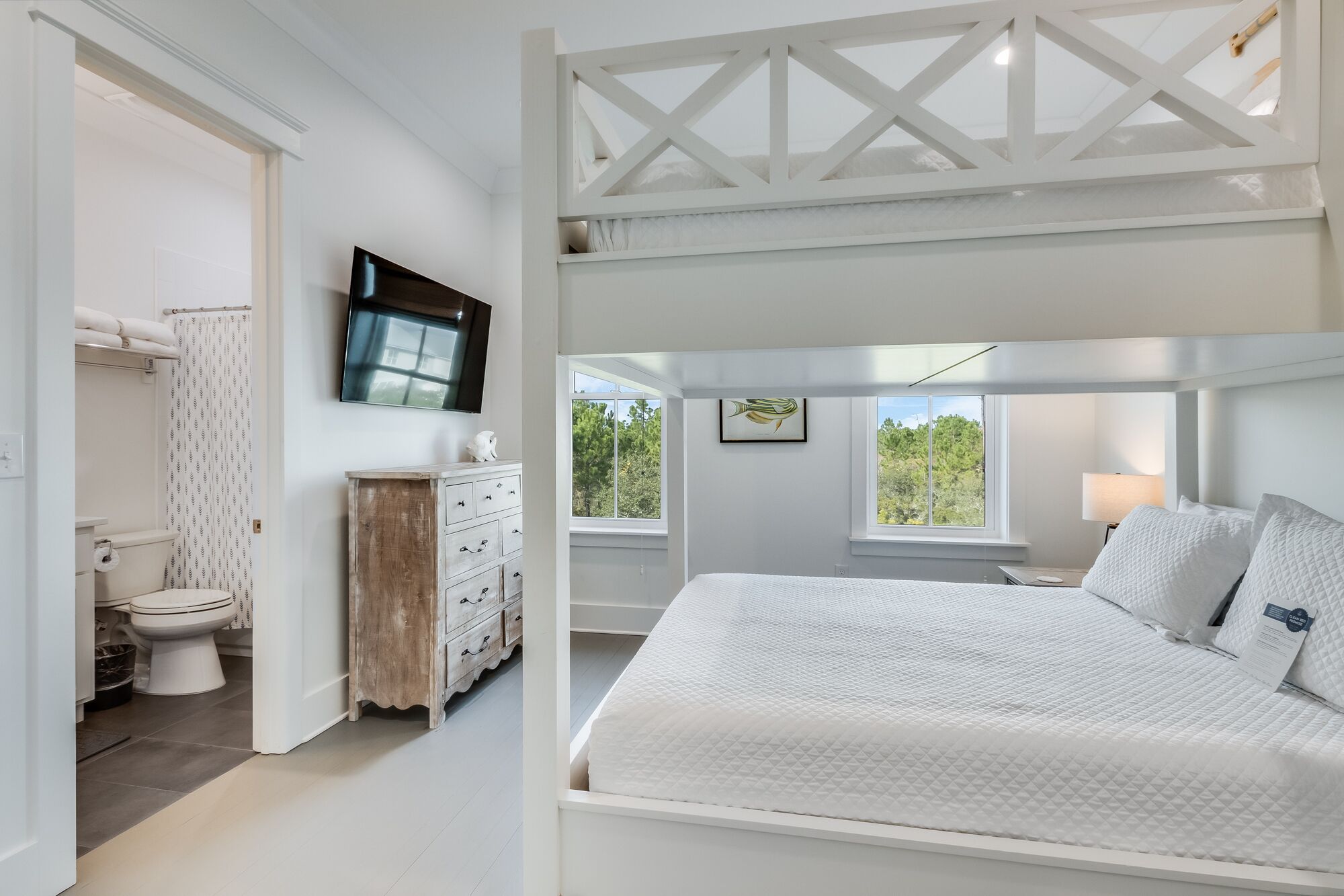 A bedroom with a large bed, a dresser, a TV, and a window with a view of trees.