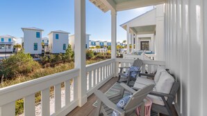 Un porche cubierto con mobiliario exterior, con vistas a una hilera de casas de playa.