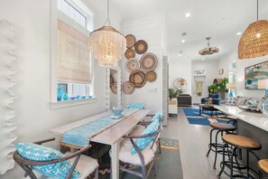 A modern kitchen with a dining area, featuring a long wooden table, bar stools, and decorative wall art.