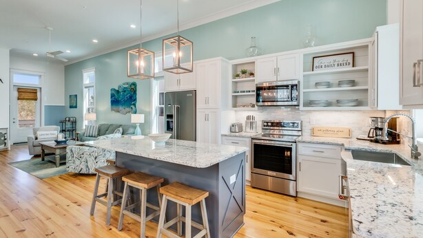 A modern kitchen with a central island, stainless steel appliances, and a dining area with a sofa and bar stools.