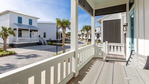 A covered porch with a wooden floor, white railings, and a view of adjacent buildings.