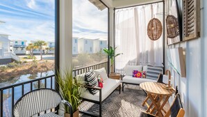 A balcony with a view of other buildings, a sofa, a chair, a small table, and a hanging light fixture.